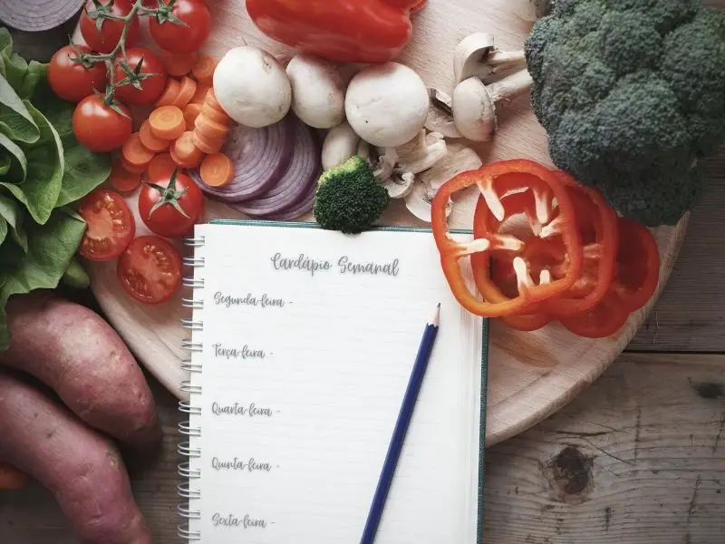 Legumes, verduras em uma tábua com um caderno e lápis - como montar um cardápio semanal