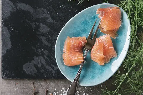 Pedaços de salmão cru em um prato azul com folhas de tempero dill

