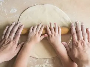 Mãos de criança e pai abrindo uma massa com rolo de macarrão